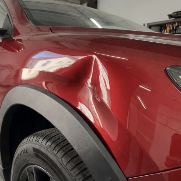 Sharp dent on a red SUV's fender — smoothed back to a flawless factory finish with paintless dent repair. — before