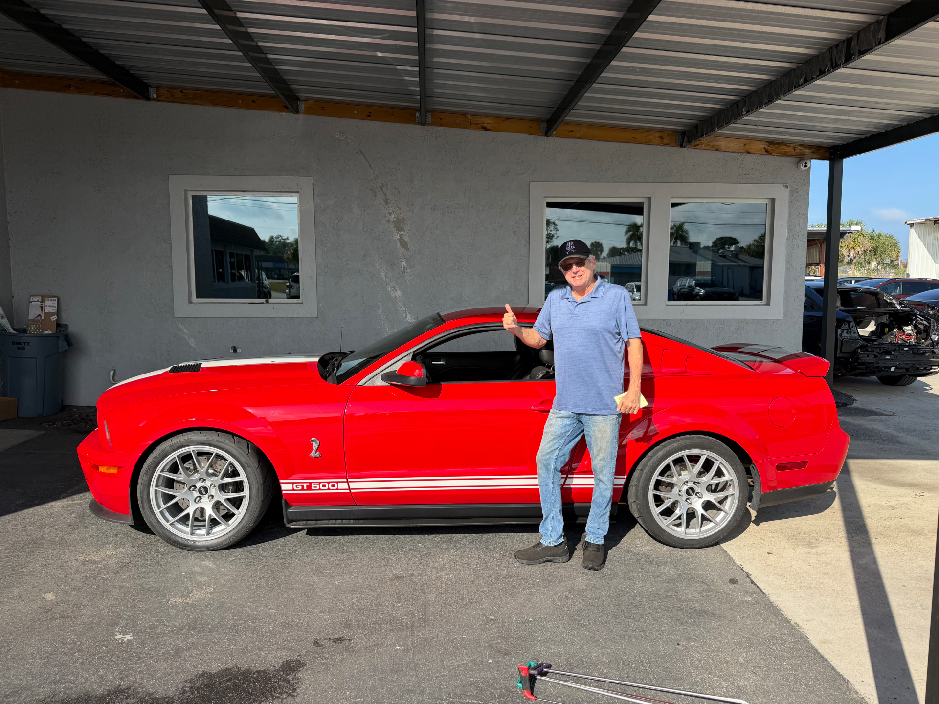 Happy Dents Now customer giving a thumbs up next to his red Shelby GT500 Mustang