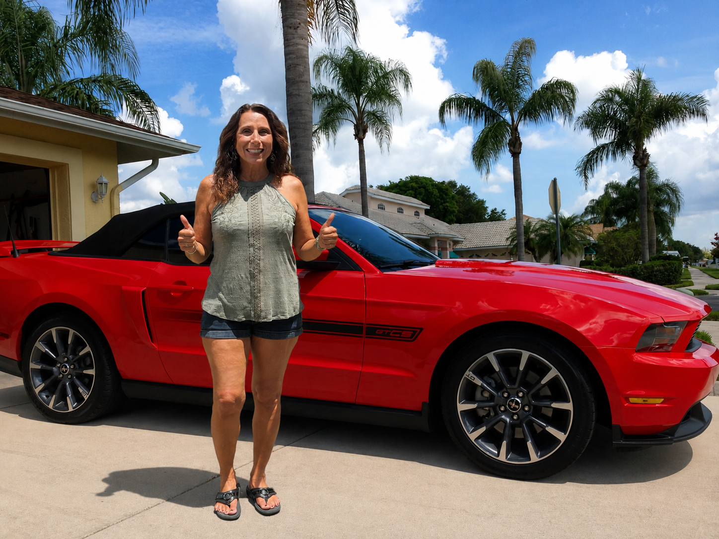 Happy Dents Now customer giving two thumbs up next to her red Ford Mustang GT/CS convertible