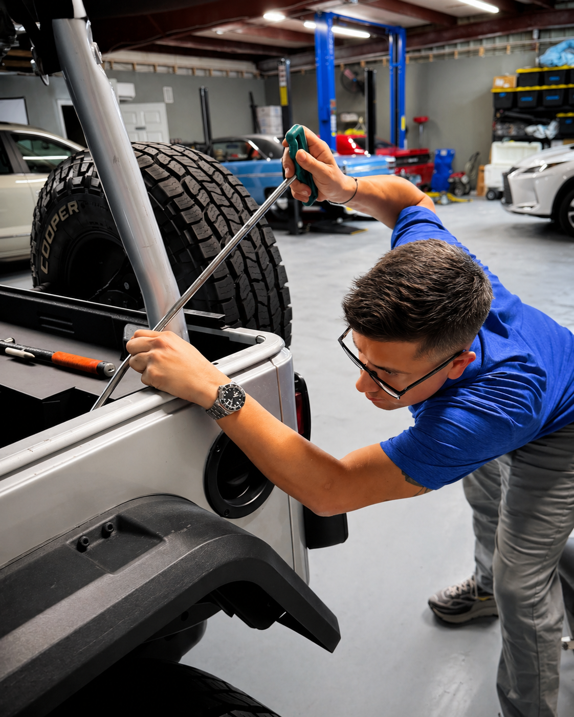 Dents Now technician using a PDR rod on a silver Jeep tailgate inside the shop